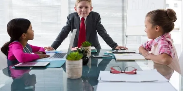 A young boy in suit and tie at desk with plants.